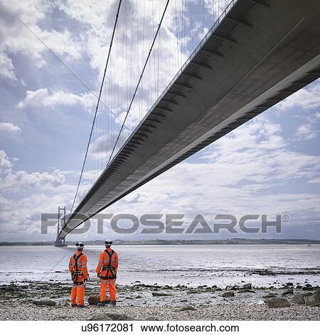 Stock Image - Bridge workers on beach under suspension bridge. The Humber Bridge, UK was built in 1981 and at the time was the world's largest single-span suspension bridge. Fotosearch
