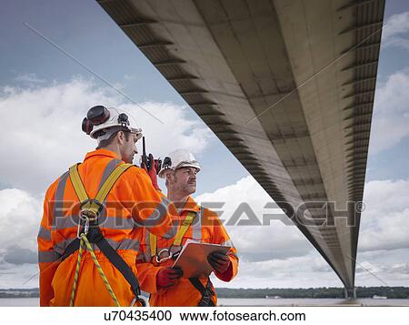 Stock Image - Bridge workers using walkie-talkie under suspension bridge. The Humber Bridge, UK was built in 1981 and at the time was the world's largest single-span suspension bridge. Fotosearch