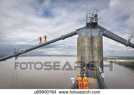Picture - Bridge workers walking on cable of suspension bridge. The Humber Bridge, UK was built in 1981 and at the time was the world's largest single-span suspension bridge. Fotosearch