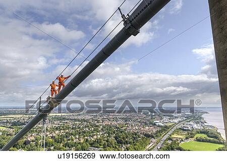 Stock Photo - Bridge workers walking on cable of suspension bridge. The Humber Bridge, UK was built in 1981 and at the time was the world's largest single-span suspension bridge. Fotosearch