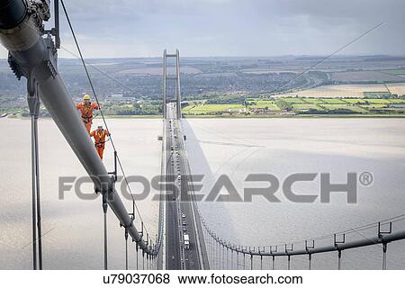 Stock Photo - Bridge workers walking on cable of suspension bridge. The Humber Bridge, UK was built in 1981 and at the time was the world's largest single-span suspension bridge. Fotosearch