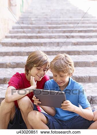 Stock Image - Brothers looking at digital tablet on village steps, Majorca, Spain. Fotosearch