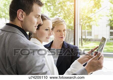 Stock Image - Businessman and businesswomen sharing information on digital tablet. Fotosearch