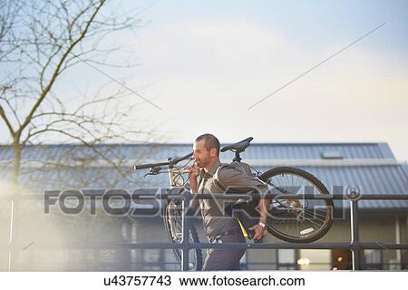 Stock Image - Businessman running with bicycle and folder in arms. Fotosearch