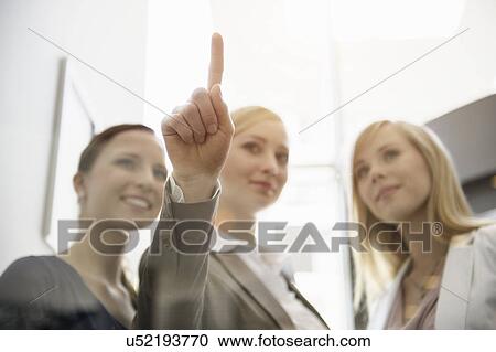 Stock Image - Businesswomen looking and pointing on glass. Fotosearch