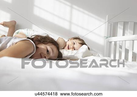 Stock Photo - Candid portrait of female toddler and cousin lying on bed. Fotosearch