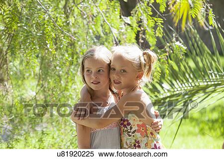 Stock Photography - Candid portrait of two girls with arms around each other in garden. Fotosearch