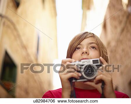 Stock Photograph - Close up of boy photographing village street using SLR camera, Majorca, Spain. Fotosearch