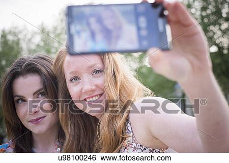 Close up of two young female friends in park taking selfie on smartphone View Large Photo Image Stock Photograph - Close up of two young female friends in park taking selfie on smartphone. Fotosearch
