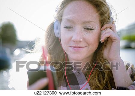 Close up of young woman listening to music on headphones on street View Large Photo Image Stock Image - Close up of young woman listening to music on headphones on street. Fotosearch
