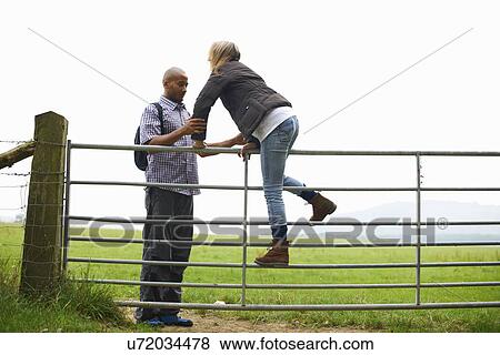 Couple climbing over gate in fields View Large Photo Image Stock Photo - Couple climbing over gate in fields. Fotosearch