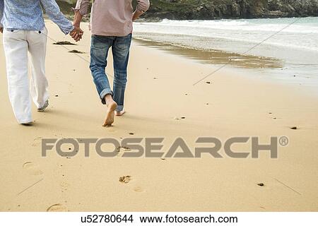 Picture - Cropped shot of mature couple holding hands whilst strolling on beach, Camaret-sur-mer, Brittany, France. Fotosearch