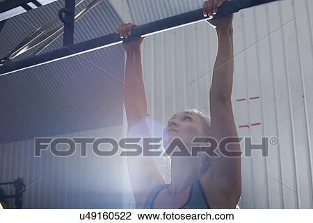 Stock Image - Crossfitter doing pull ups in gym. Fotosearch