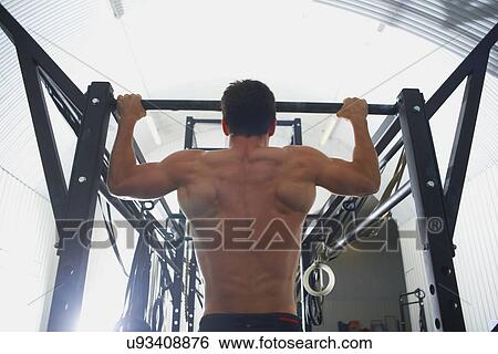 Stock Photograph - Crossfitter doing pull ups in gym. Fotosearch