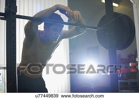Stock Photo - Crossfitter leaning on barbells in gym. Fotosearch