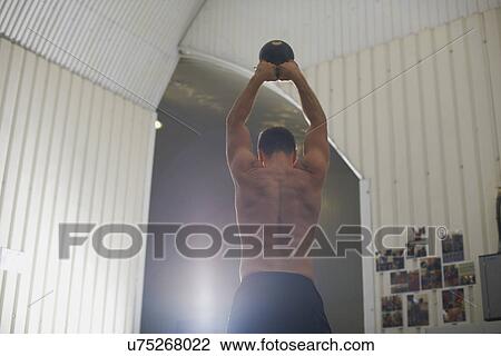 Stock Image - Crossfitter lifting kettlebell in gym. Fotosearch