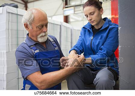 Picture - Factory worker applying first aid to colleague. Fotosearch