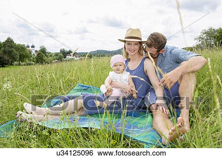Stock Photograph - Family sitting on blanket in field, portrait. Fotosearch