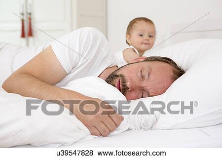 Father asleep in bed, baby daughter watching View Large Photo Image Stock Photo - Father asleep in bed, baby daughter watching. Fotosearch
