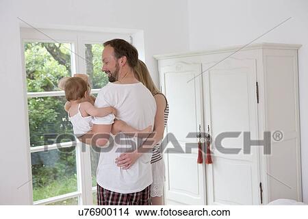 Father holding baby daughter, woman with arm around man View Large Photo Image Picture - Father holding baby daughter, woman with arm around man. Fotosearch