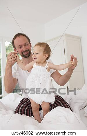 Stock Image - Father playing with baby daughter on bed. Fotosearch