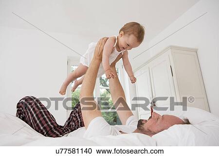 Stock Image - Father playing with baby daughter on bed. Fotosearch