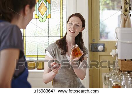 Stock Photo - Female beekeepers in kitchen, bottling filtered honey from beehive. Fotosearch