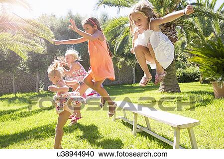 Stock Image - Five energetic girls jumping from garden bench. Fotosearch