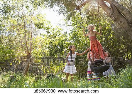 Stock Image - Four girls playing on tree tire swing in garden. Fotosearch