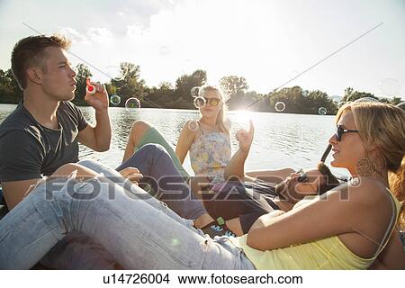 Four young adult friends blowing bubbles on riverside pier View Large Photo Image Picture - Four young adult friends blowing bubbles on riverside pier. Fotosearch