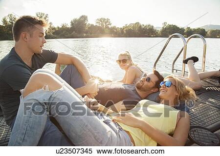 Stock Photography - Four young adult friends chatting on riverside pier. Fotosearch