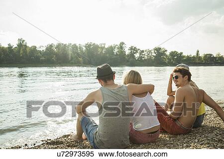Stock Photography - Four young friends sitting on lakeshore. Fotosearch