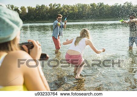 Friends playing with water pistols in lake View Large Photo Image Picture - Friends playing with water pistols in lake. Fotosearch