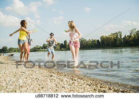 Friends playing with water pistols in lake View Large Photo Image Stock Image - Friends playing with water pistols in lake. Fotosearch