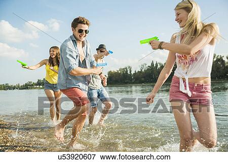 Friends playing with water pistols in lake View Large Photo Image Stock Photo - Friends playing with water pistols in lake. Fotosearch
