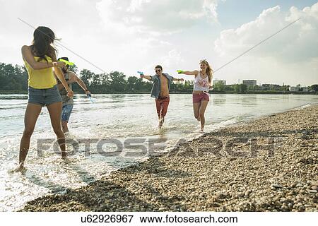 Friends playing with water pistols in lake View Large Photo Image Stock Photo - Friends playing with water pistols in lake. Fotosearch