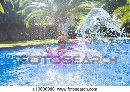 Stock Image - Girl and boy splashing around in garden swimming pool. Fotosearch