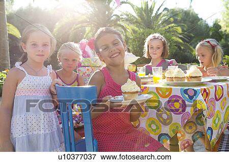 Girl at birthday party with friends holding plate with cupcake View Large Photo Image Stock Photo - Girl at birthday party with friends holding plate with cupcake. Fotosearch