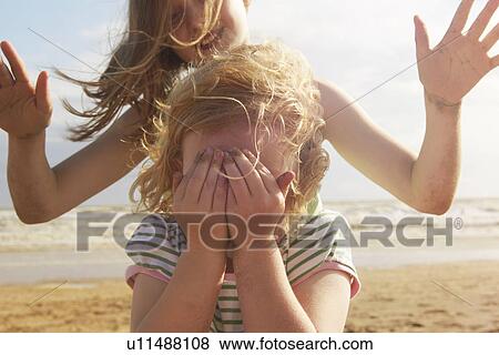 Girl covering eyes in front of sister on beach, Camber Sands, Kent, UK View Large Photo Image Stock Photo - Girl covering eyes in front of sister on beach, Camber Sands, Kent, UK. Fotosearch