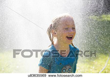 Girl getting splashed by water sprinkler in garden View Large Photo Image Stock Photo - Girl getting splashed by water sprinkler in garden. Fotosearch