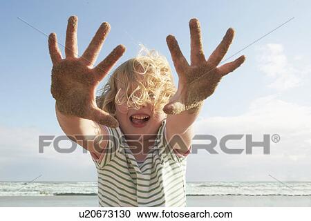 Stock Image - Girl holding up sandy hands on breezy beach, Camber Sands, Kent, UK. Fotosearch