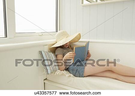 Stock Photo - Girl in sunhat reading on holiday apartment porch seat. Fotosearch