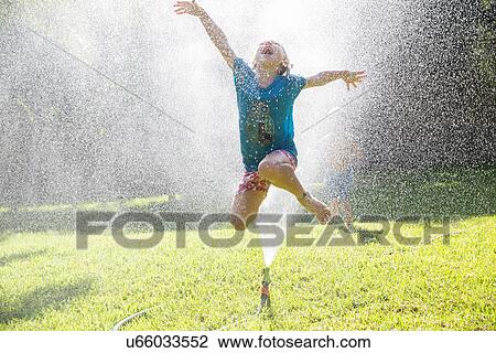 Girl jumping over water sprinkler in garden View Large Photo Image Stock Image - Girl jumping over water sprinkler in garden. Fotosearch