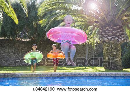 Stock Image - Girl jumping with inflatable ring into garden swimming pool. Fotosearch