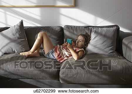 Girl lying on living room sofa playing hand held game View Large Photo Image Stock Photo - Girl lying on living room sofa playing hand held game. Fotosearch