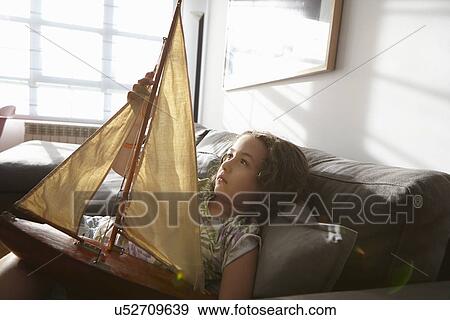 Stock Photo - Girl lying on living room sofa with toy sailing boat. Fotosearch