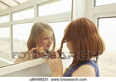 Stock Image - Girl plaiting hair in holiday apartment porch. Fotosearch