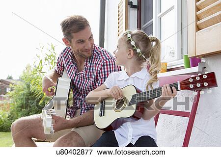 Girl playing guitar with father View Large Photo Image Stock Photo - Girl playing guitar with father. Fotosearch