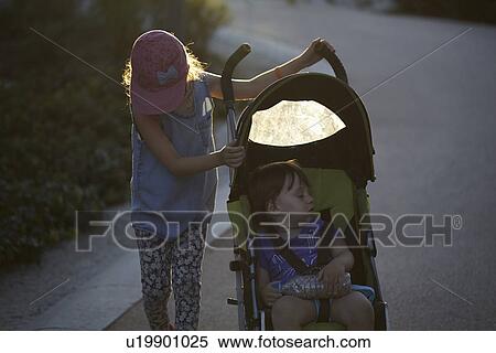 Girl pushing toddler sister in pushchair through park at sunset View Large Photo Image Stock Photography - Girl pushing toddler sister in pushchair through park at sunset. Fotosearch
