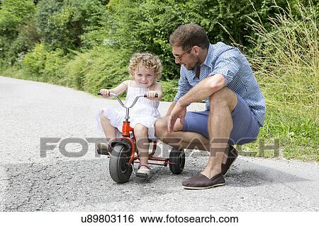 Girl riding tricycle with father View Large Photo Image Stock Photograph - Girl riding tricycle with father. Fotosearch